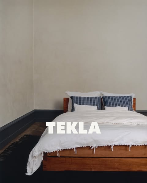 This image ad features a bed with white linens and blue plaid pillows. The name of the brand, TEKLA, is displayed in the
