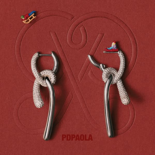 This ad showcases a pair of PDPAOLA earrings on a red background with a miniature person sitting on one of the earrings 