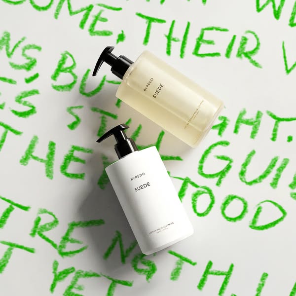 This image ad showcases two bottles of Byredo Suede lotion and hand wash against a white background scrawled with green