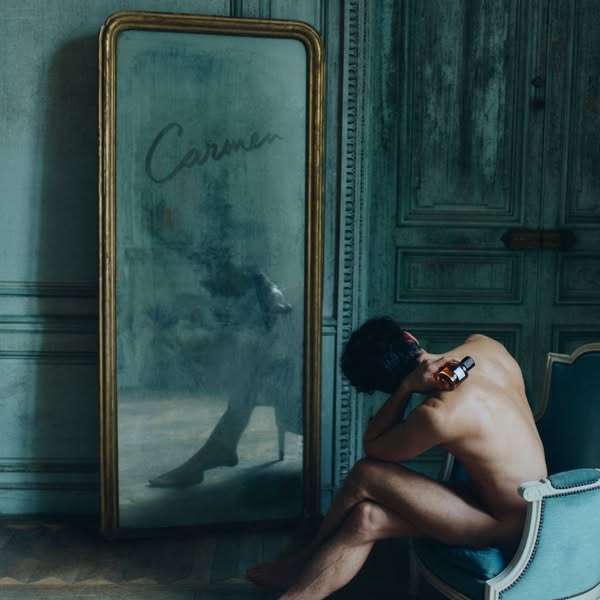 This ad features a nude man sitting in a room looking at his reflection in a mirror. He appears to be putting on or have