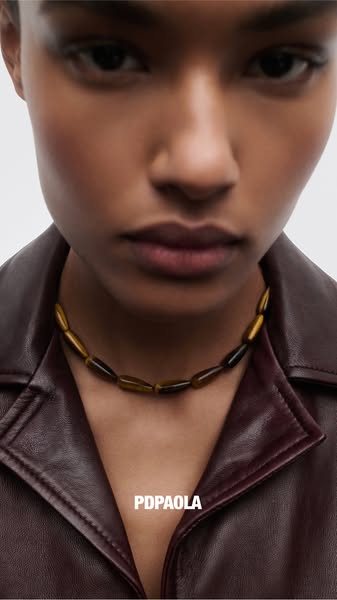 This ad features a close-up shot of a woman wearing a beaded necklace from the brand PDPAOLA. The focus is on the neckla