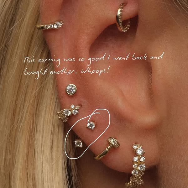 A close up image of a person's ear shows a variety of small earrings, including the specific earring the brand is tr
