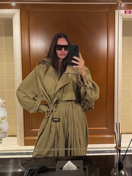 This ad features a woman taking a mirror selfie while wearing a trench coat.