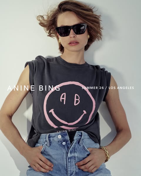 This image ad features a stylish woman wearing a black ANINE BING t-shirt with a smiley face logo and light wash denim s