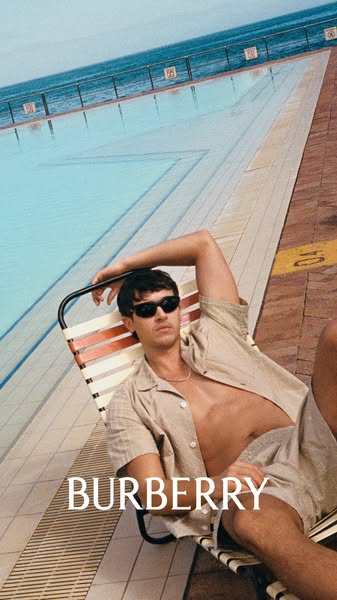 A fashion ad that features a man laying on a lounge chair by a pool wearing matching shirt and shorts.