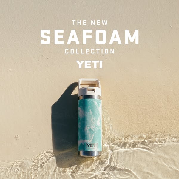 This ad showcases a YETI water bottle in the new Seafoam collection. The bottle is positioned on a sandy beach, partiall