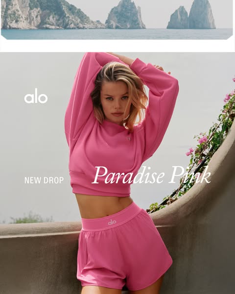 This image ad promotes Alo Yoga apparel, specifically a pink sweatshirt and shorts set. It uses a background image of a 