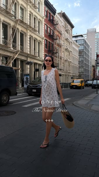 This is a product showcase ad that highlights a dress from the brand Doen. The ad shows a model in a city wearing the dr
