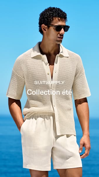 An image showing a male model wearing a beige knitted short sleeve shirt and matching beige shorts in front of a blue ba