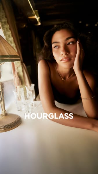 This image ad by Hourglass features a woman sitting at a table with the Hourglass logo displayed at the bottom.