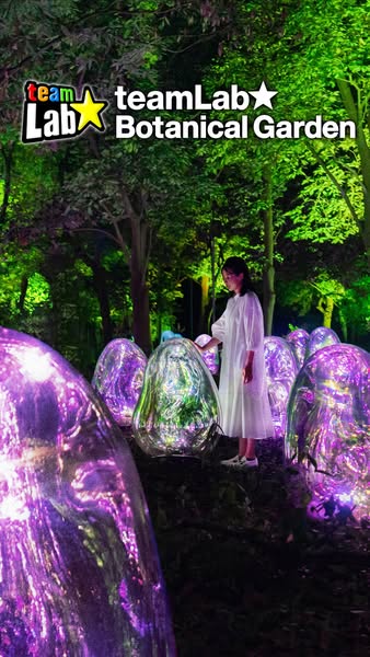 This ad showcases the TeamLab Botanical Garden, featuring a woman interacting with the illuminated egg-shaped structures
