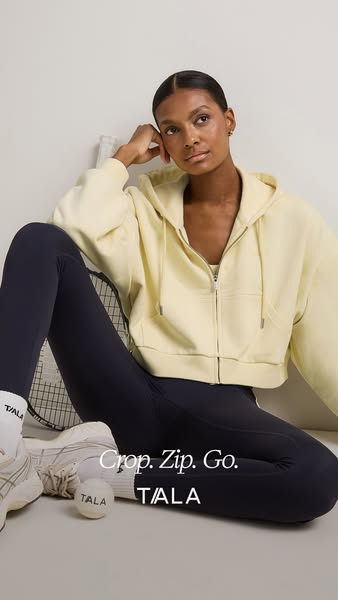 This image ad features a woman wearing apparel by TALA. The woman is wearing the black leggings and a light yellow zip u