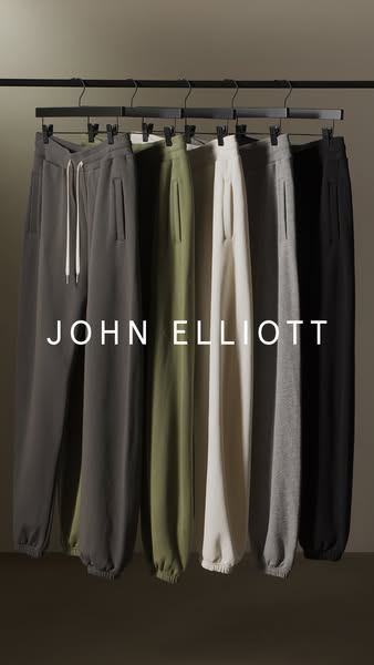 This ad showcases a variety of sweatpants from the brand John Elliott. The sweatpants are hung on a rack and are in diff