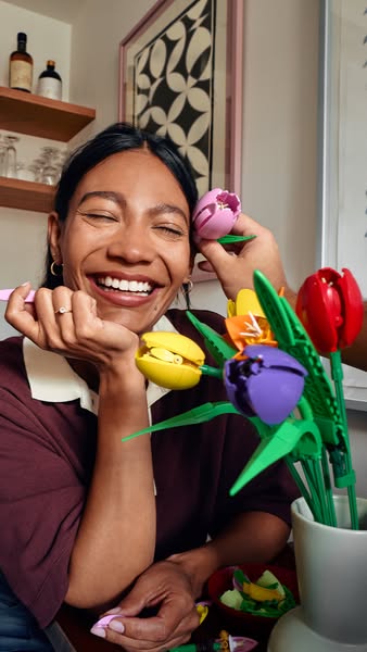 A social media image ad features a smiling woman holding a LEGO flower set. The ad promotes the joy and creativity that 