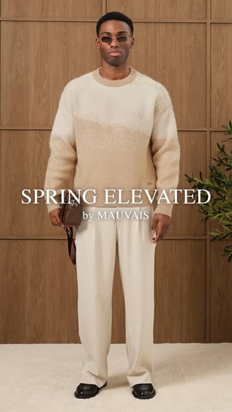 A full body shot of a male model wearing MAUVAIS sweater and pants and holding a small bag is shown.