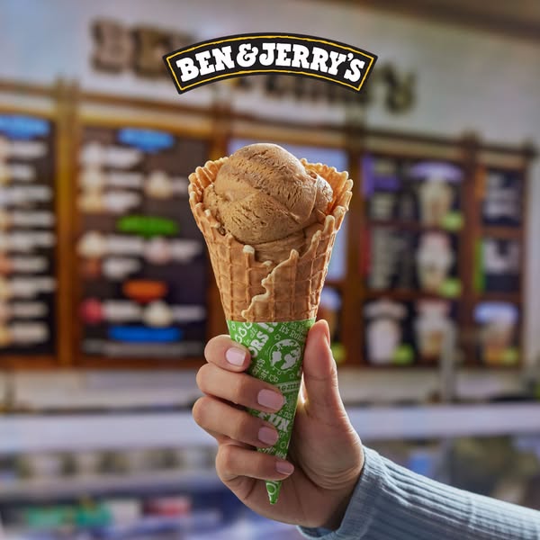 A cone of Ben & Jerry's ice cream is displayed in front of a Ben & Jerry's storefront. The ice cream con