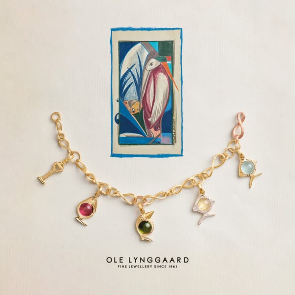 This ad features a gold charm necklace with gemstone pendants against a white background with a framed illustration.