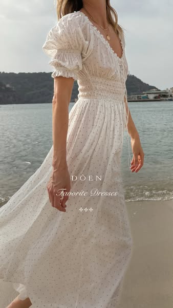 This ad showcases a woman wearing a white and blue dress while standing on a beach. The ad is for Doen and features thei