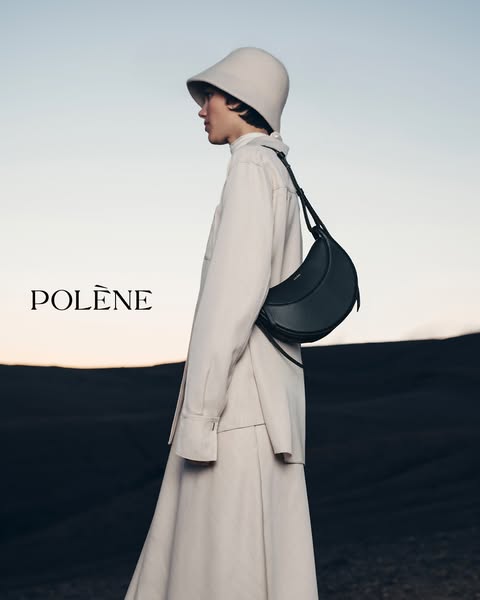 This ad features a woman modeling the Polène bag. She is standing in an open, natural setting at dusk.