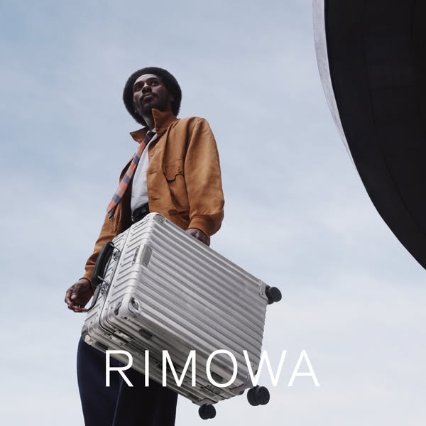 A low angle shot of a person holding a Rimowa suitcase with the brand name at the bottom.