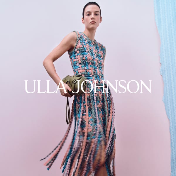 This Ulla Johnson ad features a model in a woven dress with fringe, holding a green woven bag against a light pink backd