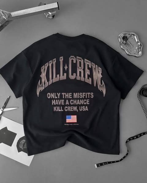 A flatlay product image ad for the clothing brand KILL CREW featuring one of their t-shirts. The t-shirt is black and ha