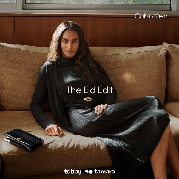 This ad for Tabby and Tamara features a woman sitting on a couch wearing a black pleated dress and cardigan from the Cal