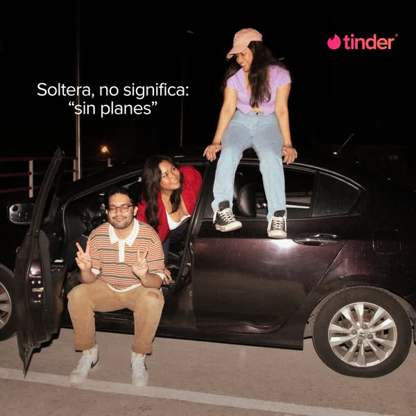 This Tinder ad uses an image of three young adults standing and sitting around a car at night. The ad is in Spanish and 
