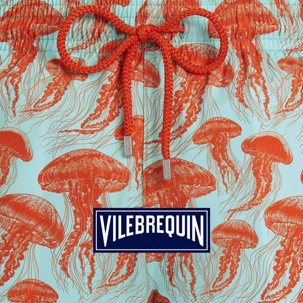 This ad features Vilebrequin swim trunks. The trunks have a pattern of orange jellyfish on a light blue background. The 
