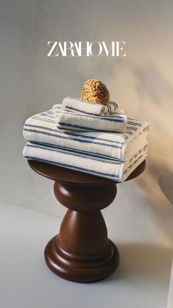 This is a product image promoting towels from Zara Home. A stack of folded striped towels is arranged on a decorative wo