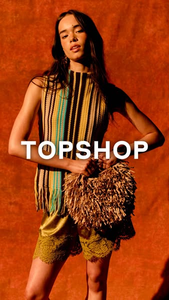 This ad for Topshop features a stylish woman in a striped top and shorts, holding a shaggy straw-like bag, against an or