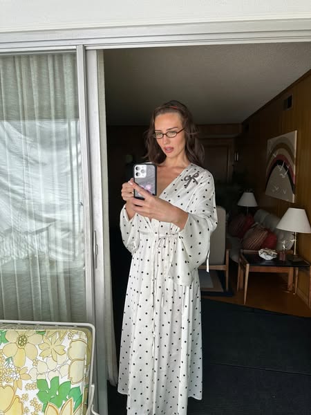 A lifestyle photograph features a woman indoors holding a cell phone. She is wearing a white polka dot robe. The ad is l