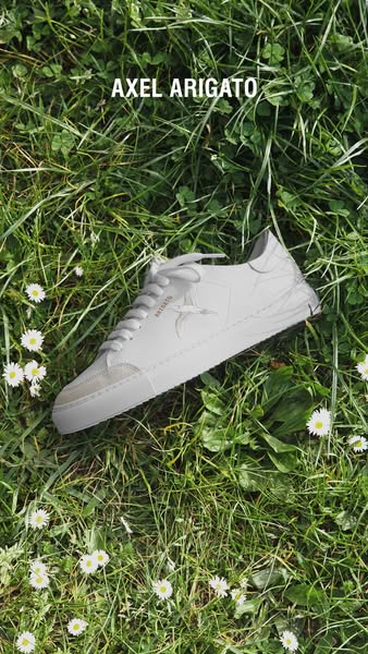 An ad showcasing a white sneaker from the brand Axel Arigato, placed in grass.