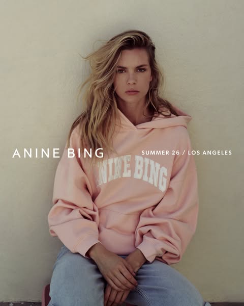 This ad features a person with long blonde hair sitting on a pink stool. She is wearing a light pink hooded sweatshirt w