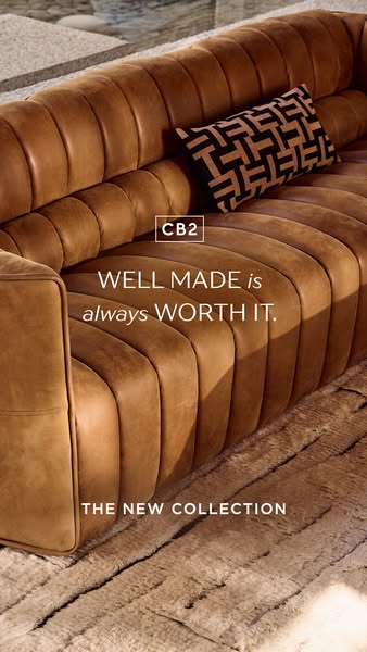 This image ad for CB2 features a close-up shot of a brown leather couch with a patterned pillow. The ad highlights the b