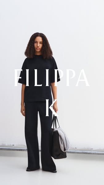 A woman in a black loungewear outfit stands in front of a white wall. The brand's name is superimposed over the imag
