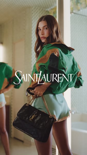 This ad features Hailey Bieber showcasing a Saint Laurent purse in front of a mirror.