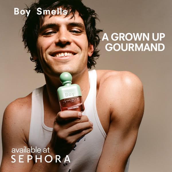 This image ad promotes Boy Smells Coco Hinoki fragrance. It features a smiling individual holding the product bottle, wi