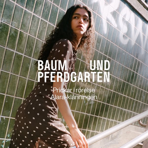 An image ad for Baum Und Pferdgarten features a person standing on stairs and wearing a polka dot dress from the brand. 
