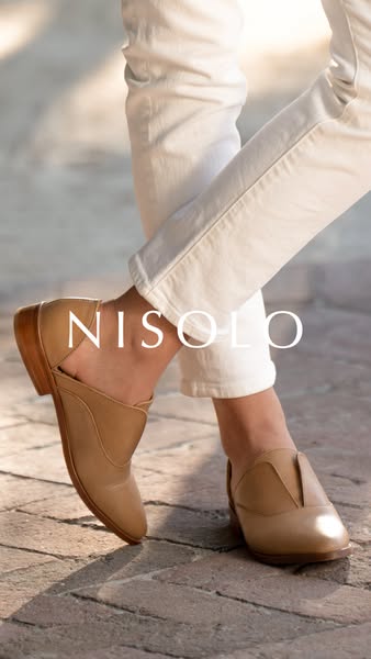 A fashionable pair of Nisolo mules is presented on a stone floor.
