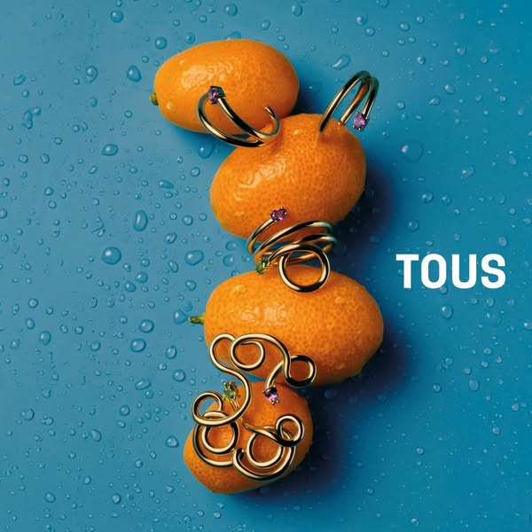 The ad features gold-tone jewelry from TOUS set against a blue background with water droplets, styled alongside fresh ku