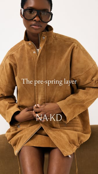 A medium shot of a woman wearing a brown suede jacket and matching skirt, zipped slightly open, paired with large framed