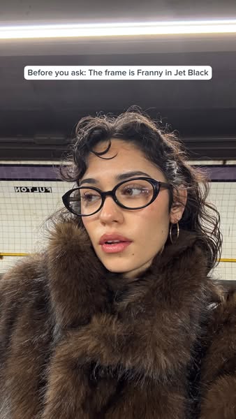 The ad features a woman wearing black cat eye glasses in an indoor setting with subway tiles and track lighting visible 