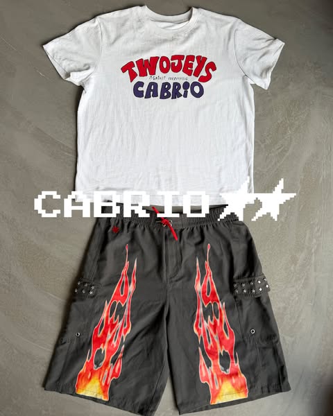 This ad features a white t-shirt and gray shorts with flames on them laid out on a gray background. The word "CABRI