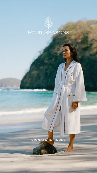 This ad showcases a woman on a beach wearing a white robe with black trim. The ad is for Four Seasons signature robes.