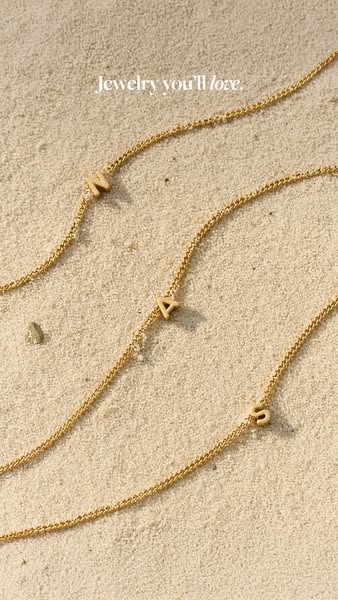 The image ad showcases three gold initial necklaces on a sandy background, with the headline "Jewelry you'll lo