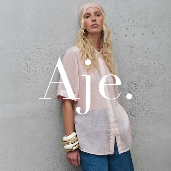 This ad showcases the brand Aje. and features a model wearing a pink button-down shirt and blue jeans.