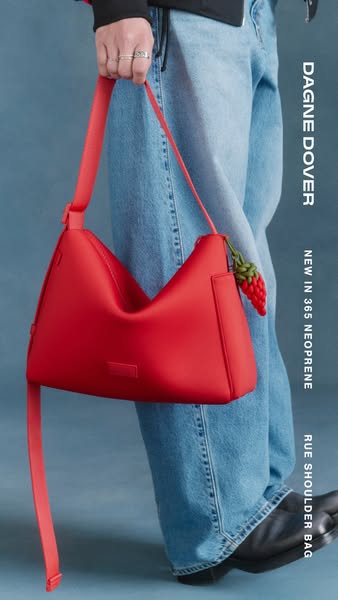 This image ad showcases a single red Dagne Dover Rue Shoulder Bag on the arm of someone wearing jeans and black shoes. T