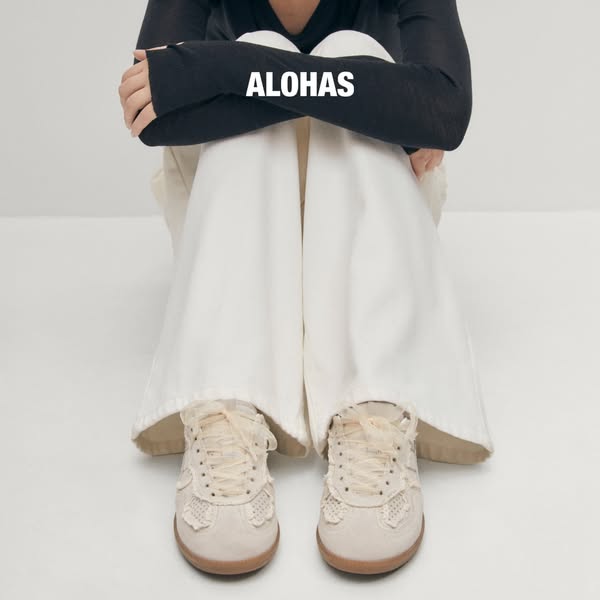 This image ad features a person sitting with their knees up to their chest, wearing white ALOHAS sneakers. The brand nam