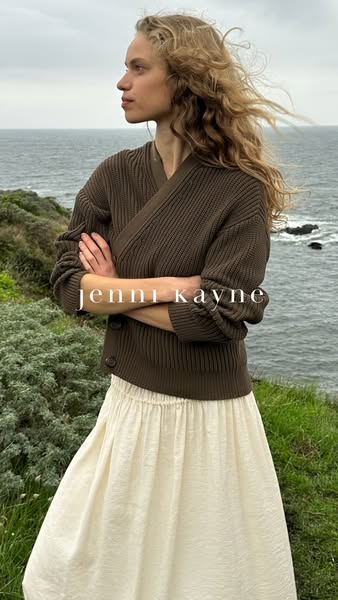 This ad features a woman modeling a Jenni Kayne cardigan and skirt set by the ocean.